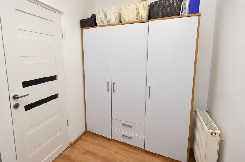 Weißer Schrank mit Körben, Türen und Boden mit Holzdekor in einer Einzimmerwohnung.