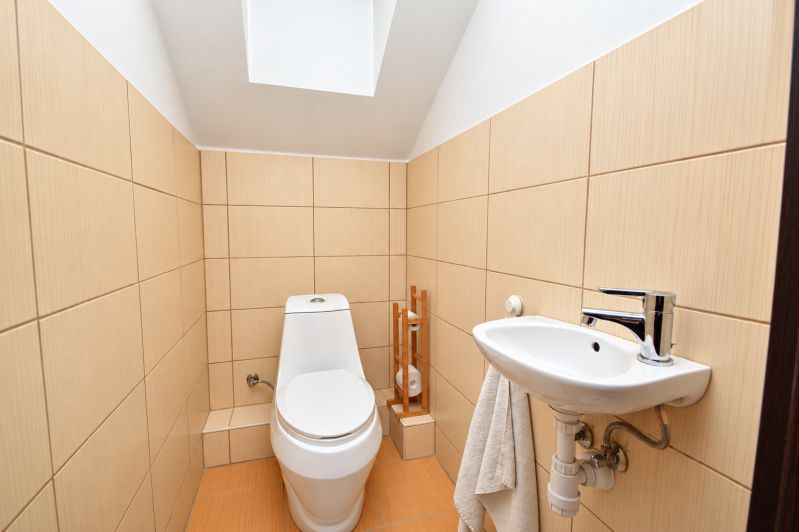 Badezimmer im Einfamilienhaus mit Toilette und Waschbecken, beige Fliesen.