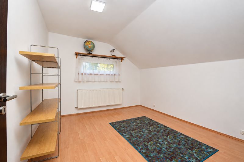 Ein Zimmer in einem Einfamilienhaus mit einem Boden in Holzoptik, einem Regal und einem Fenster.