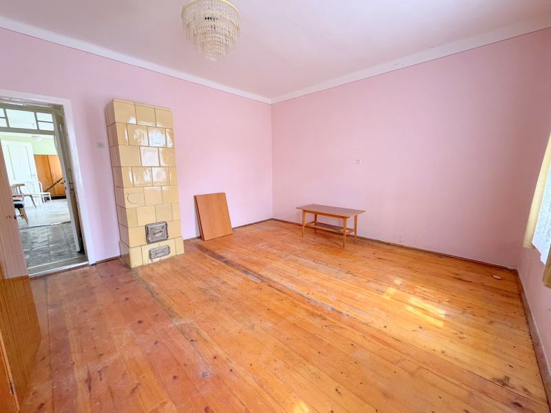 Ein Zimmer in einem Einfamilienhaus mit einem Kachelofen und einem Boden in Holzoptik.
