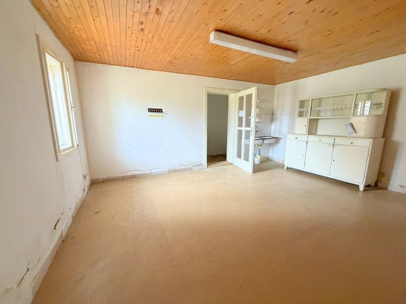 Das Innere eines Einfamilienhauses mit Holzbalkendecke, alten Möbeln und weißen Wänden.