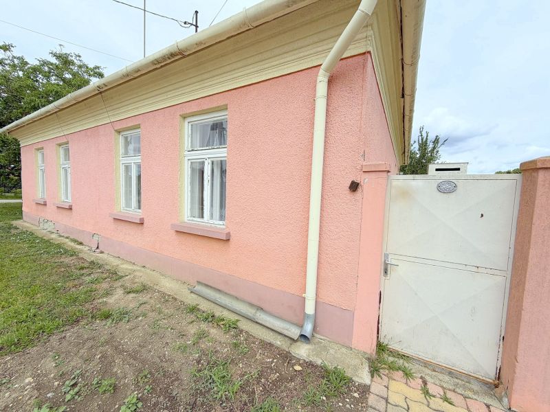 Ein Einfamilienhaus in Dunakiliti mit rosa Fassade, weißen Fenstern und einem Tor.