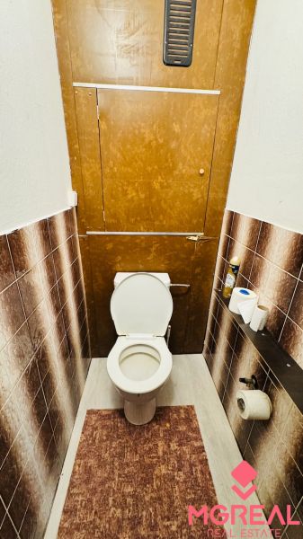 Toilette in einer 3-Zimmer-Wohnung mit braunen Fliesen und einer Fußmatte.