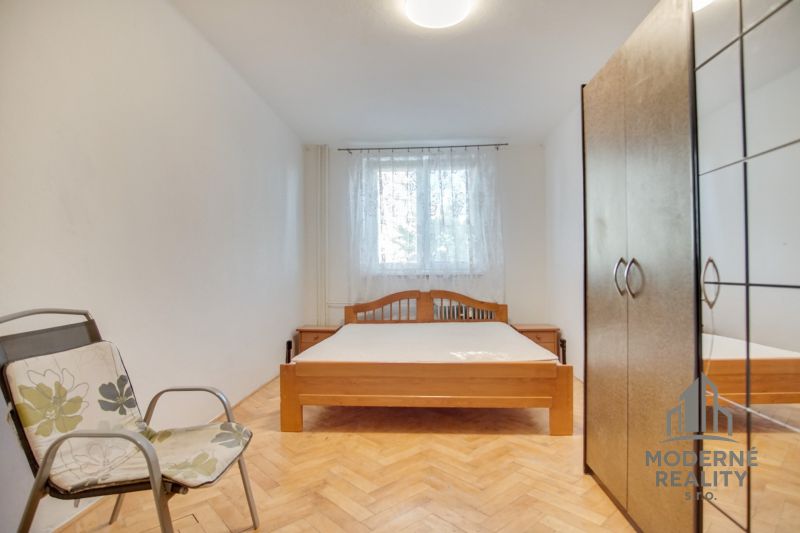 Schlafzimmer in einer 2-Zimmer-Wohnung mit einem Doppelbett, einem Stuhl und einem Boden mit Holzdekor.