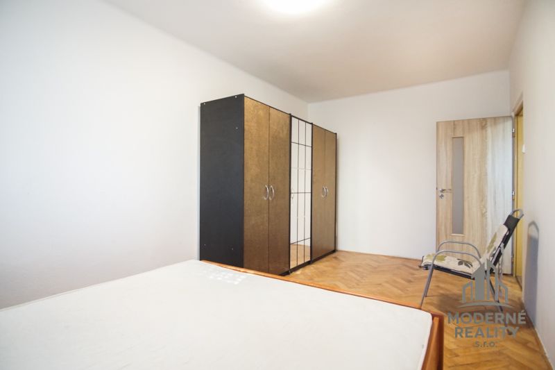 Schlafzimmer mit Kleiderschrank, Bett und Boden mit Holzdekor in einer 2-Zimmer-Wohnung.