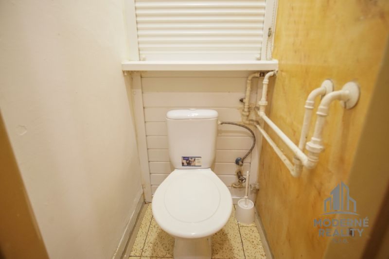 Ein kleines Badezimmer in einer 2-Zimmer-Wohnung mit Toilette, weißen Wänden und Rohren an der Seitenwand.