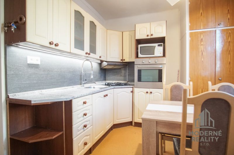 Küche in einer 2-Zimmer-Wohnung mit weißen Schränken und einem Esstisch.