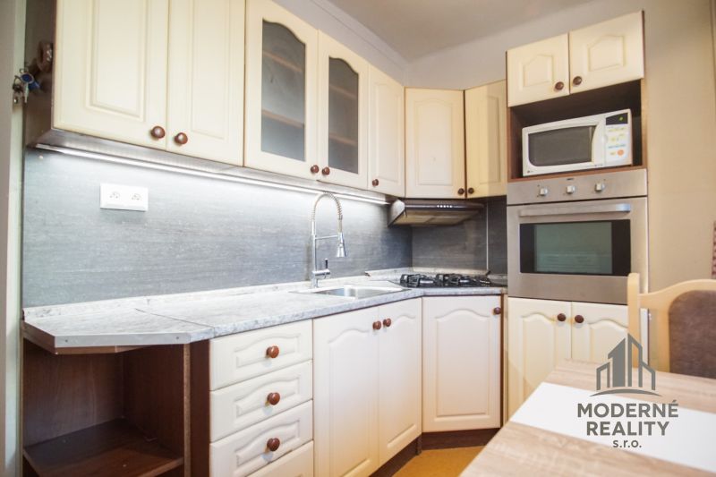 Küche in einer 2-Zimmer-Wohnung mit weißen Schränken und eingebauten Geräten.