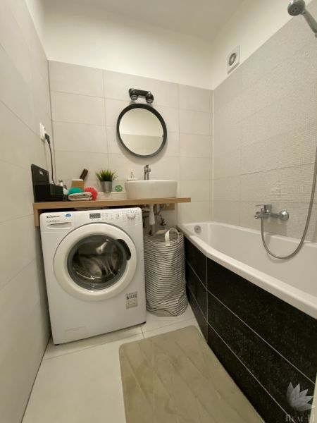 Badezimmer einer 3-Zimmer-Wohnung mit Waschmaschine, Badewanne, Waschbecken und rundem Spiegel.