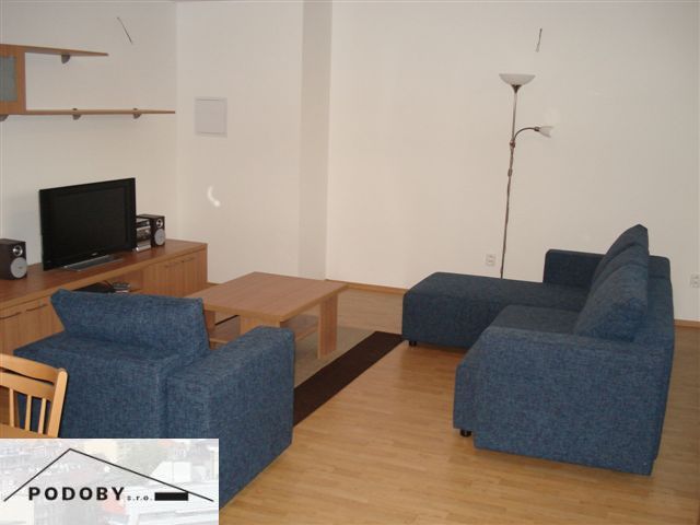 Wohnzimmer in einer 3-Zimmer-Wohnung mit einem blauen Sofa und einem Boden in Holzoptik.