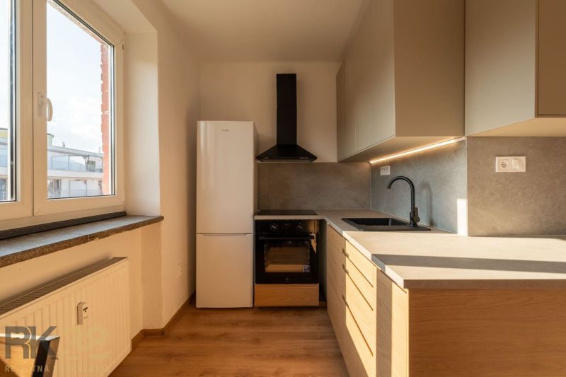 Küche in einer Einzimmerwohnung mit Küchenzeile, Boden in Holzoptik und Fenster.