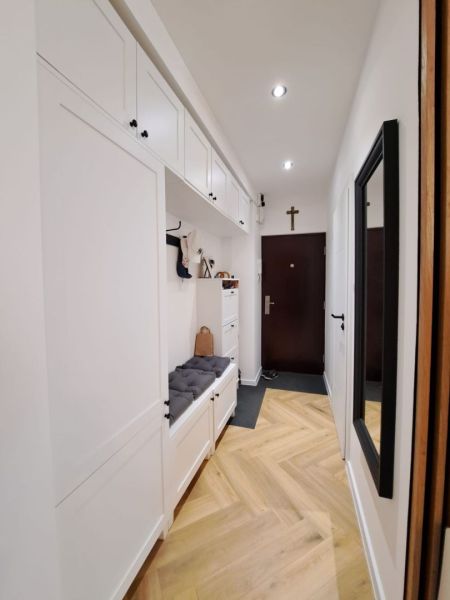 Der Flur in einer 3-Zimmer-Wohnung mit einem Boden in Holzoptik und weißen Aufbewahrungsschränken.