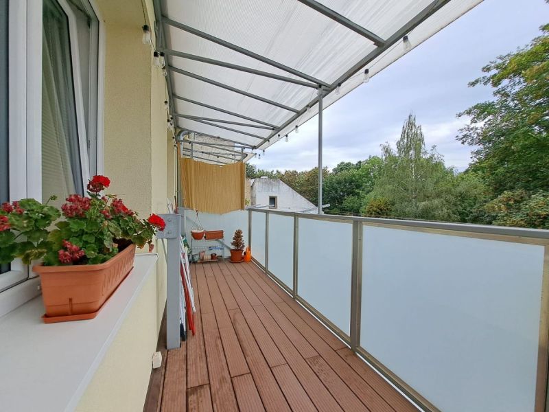 Ein Balkon in einer 3-Zimmer-Wohnung mit Holzboden, Blumen und Aussicht.