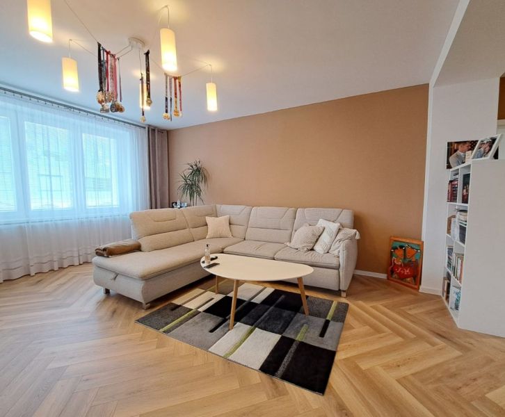 Wohnzimmer in einer 3-Zimmer-Wohnung mit einem weißen Sofa und einem Boden in Holzoptik.