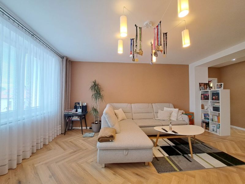 Wohnzimmer mit weißem Sofa, Holzboden und Bücherregal in einer 3-Zimmer-Wohnung.