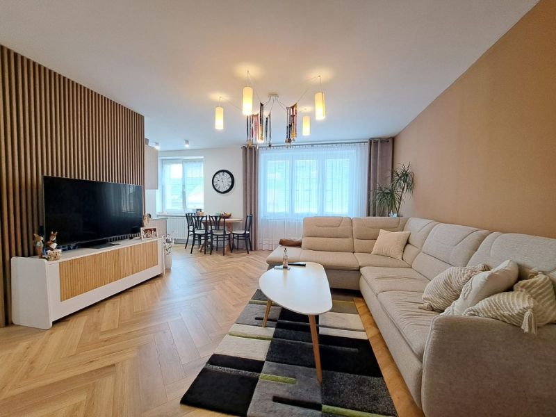 Wohnzimmer in einer 3-Zimmer-Wohnung mit Sofa, Holzelementen und Esstisch im Hintergrund.