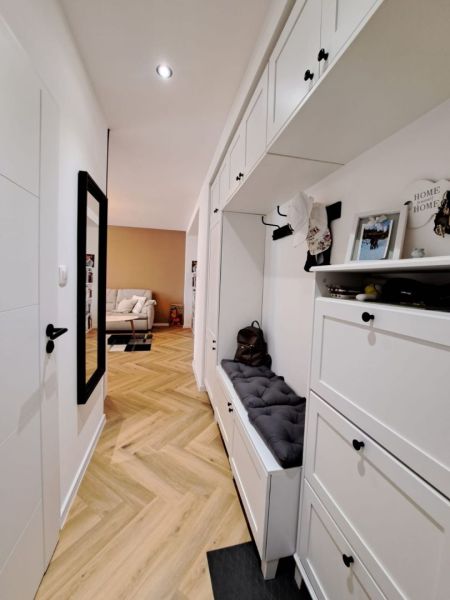Der Flur in einer 3-Zimmer-Wohnung mit weißen Möbeln und einem Boden in Holzoptik.
