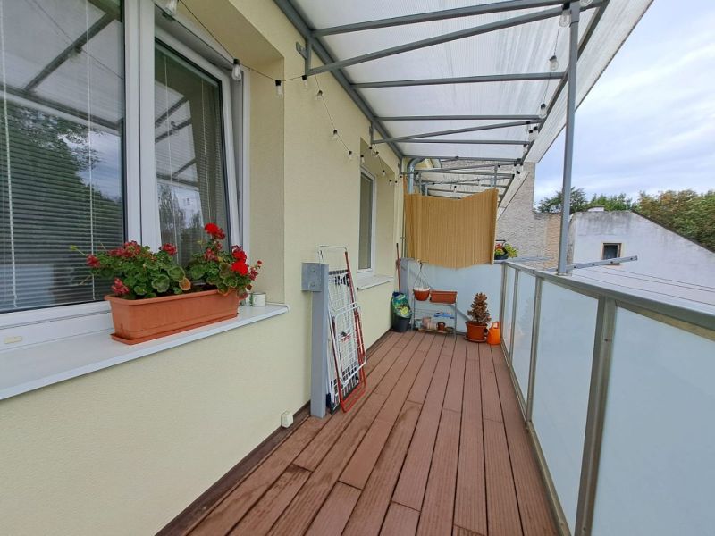 Balkon einer 3-Zimmer-Wohnung mit Holzboden, Blumenkasten und Wäschetrockner.