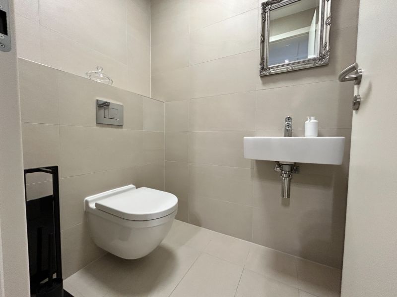 Toilette mit Waschbecken und Spiegel in einer 2-Zimmer-Wohnung, beige Fliesen.