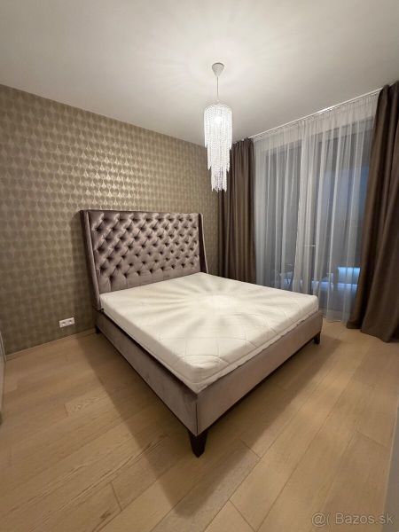 Schlafzimmer in einer 2-Zimmer-Wohnung mit Bett, Vorhängen und Boden in Holzoptik.