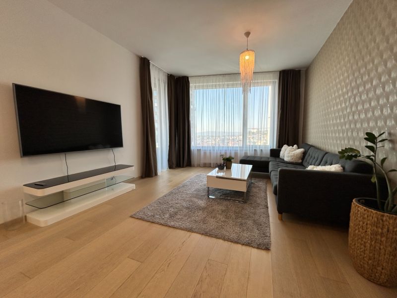 Wohnzimmer in einer 2-Zimmer-Wohnung mit Holzboden, großem Fenster und Fernseher.