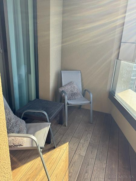 Balkon einer Zweizimmerwohnung mit Holzboden, zwei Stühlen und Glasgeländer.