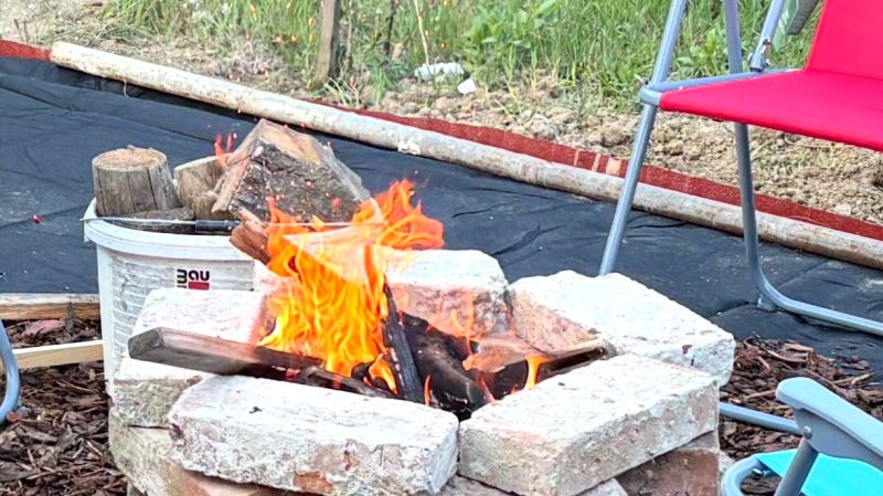 Eine Feuerstelle, umgeben von Ziegeln und Stühlen, im Garten eines Einfamilienhauses.