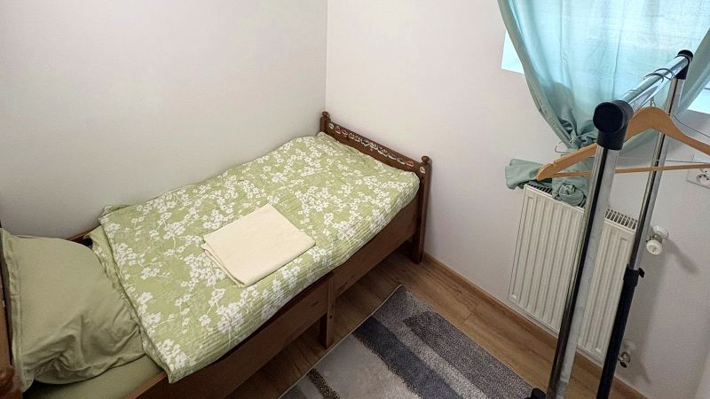 Einzelbett, Kleiderständer, grüne Vorhänge, Boden mit Holzdekor.