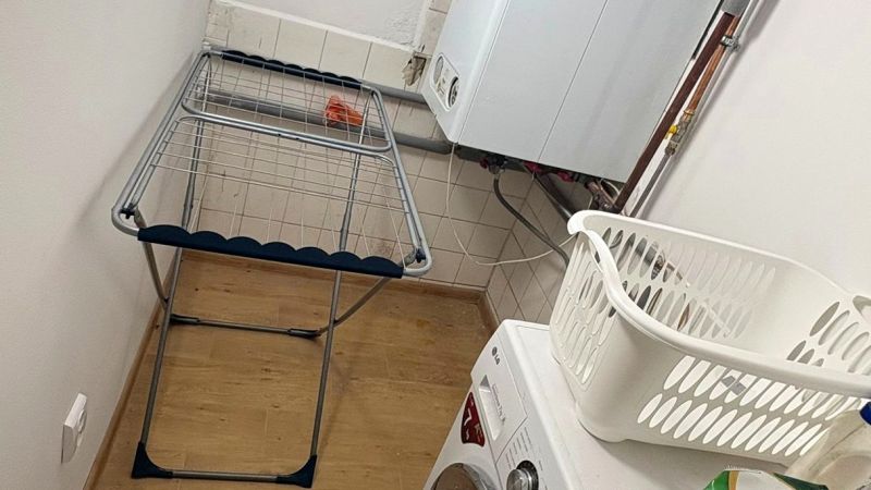 Waschküche in einem Einfamilienhaus mit Waschmaschine, Wäscheständer und Boden mit Holzdekor.