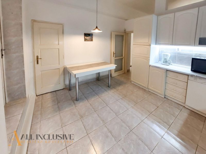 Küche in einer 2-Zimmer-Wohnung mit weißen Schränken, Tisch und Fliesen.
