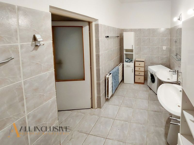 Badezimmer in einer 2-Zimmer-Wohnung mit Waschmaschine, Doppelwaschbecken und cremefarbenen Fliesen.