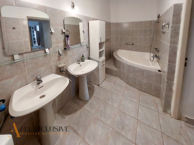 Badezimmer mit zwei Waschbecken, Eckbadewanne und hellen Fliesen in einer 2-Zimmer-Wohnung.