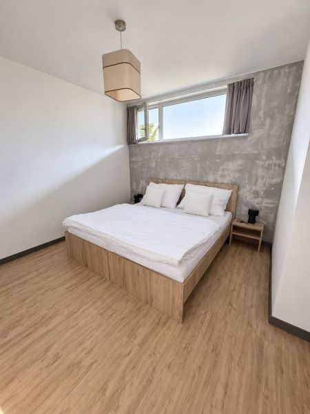 Schlafzimmer in einer 2-Zimmer-Wohnung mit Bett, grauer Wand und Boden in Holzoptik.