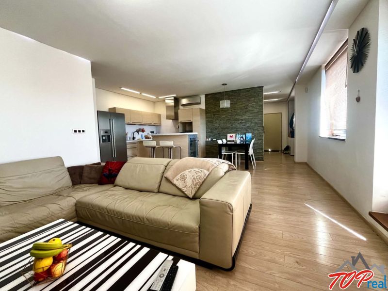 Wohnzimmer einer 3-Zimmer-Wohnung mit Holzboden und Küchenzeile.