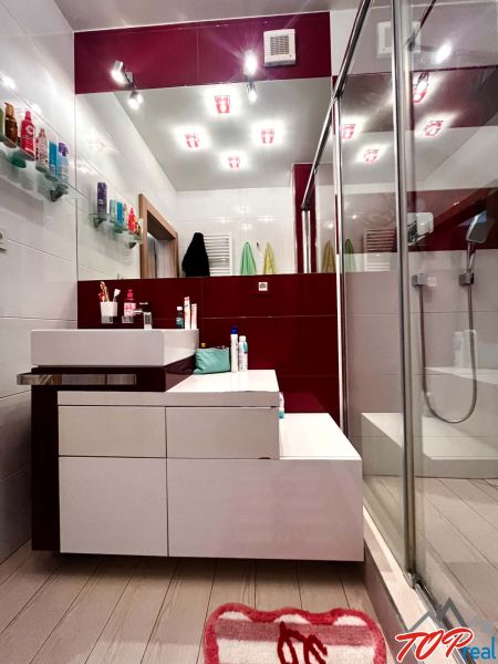 Badezimmer mit Dusche, Waschbecken und Regalen in einer 3-Zimmer-Wohnung.