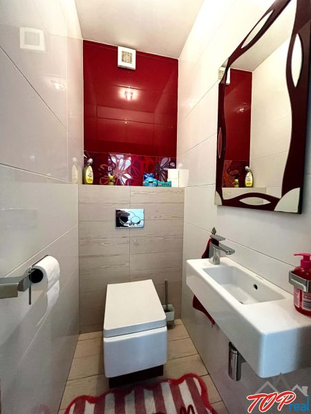 Badezimmer in einer 3-Zimmer-Wohnung mit hängendem WC, Waschbecken und roten Fliesen.