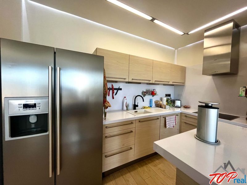 Küche in einer 3-Zimmer-Wohnung mit Holzboden, weißer Küchenzeile und Edelstahlgeräten.