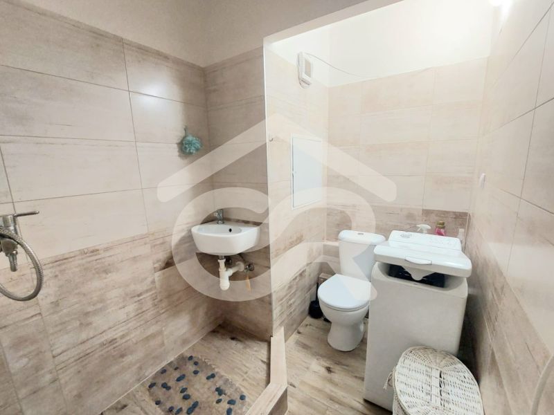Badezimmer in einem Studio-Apartment mit Toilette, Waschbecken und Waschmaschine; Boden mit Holzdekor.