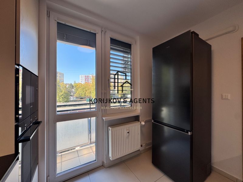 Eine Küche mit weißen Wänden, großen Fenstern und einem schwarzen Kühlschrank in einer 3-Zimmer-Wohnung.