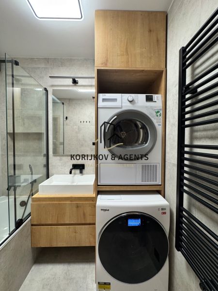 Badezimmer in einer 3-Zimmer-Wohnung mit Waschmaschine und Trockner, helle Fliesen, Holzelemente.