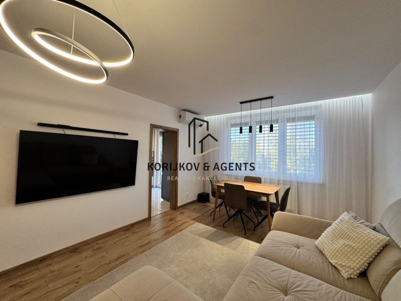 Wohnzimmer in einer 3-Zimmer-Wohnung mit einem großen Fernseher, einem Boden in Holzoptik und einem Esstisch.