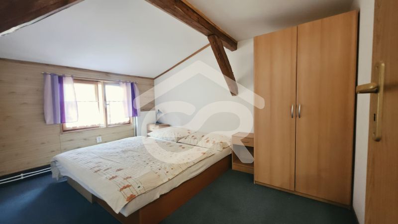 Schlafzimmer in der Ferienwohnung mit Holzbalken, Schrank und Bett neben dem Fenster.