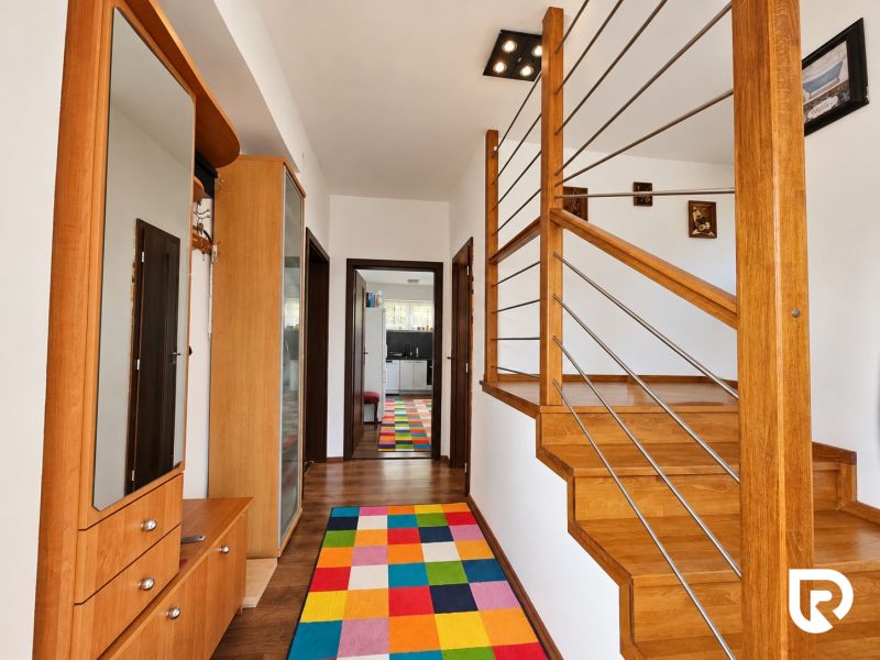 Innenraum eines Einfamilienhauses mit einer Treppe aus Holzdekor und einem bunten Teppich.