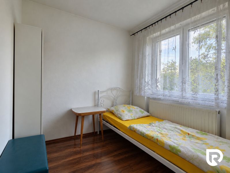 Einzelzimmer mit Bett und Tisch, Boden mit Holzdekor, weißes Interieur.