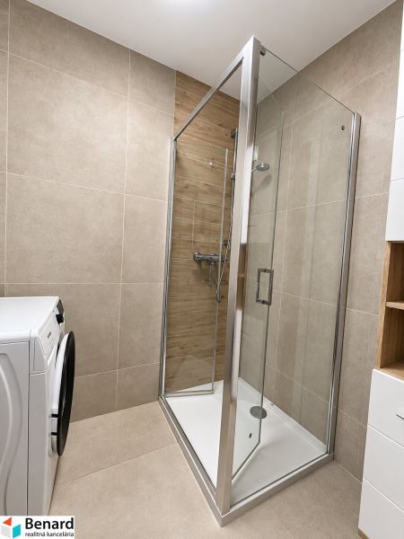 Duschkabine im Badezimmer einer 2-Zimmer-Wohnung mit Waschmaschine, Fliesen mit Holzdekor.