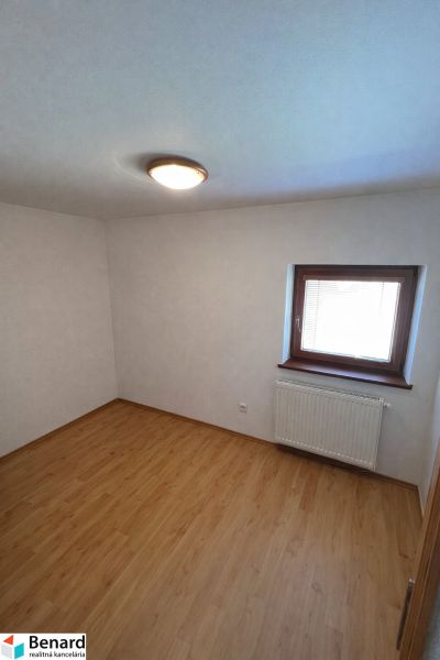 Ein Zimmer in einem Einfamilienhaus mit einem Boden in Holzoptik und einem Fenster mit Heizkörper.
