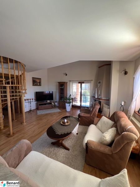 Wohnzimmer in einem Einfamilienhaus mit einem bequemen Sofa, einer Treppe und einem Boden in Holzoptik.