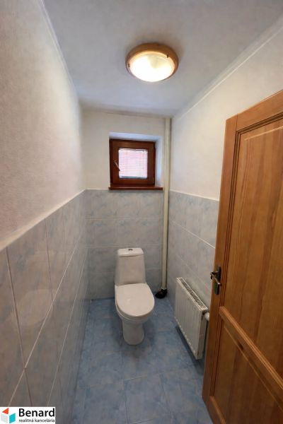 Toilette in einem Einfamilienhaus mit blauen Fliesen und kleinem Fenster.