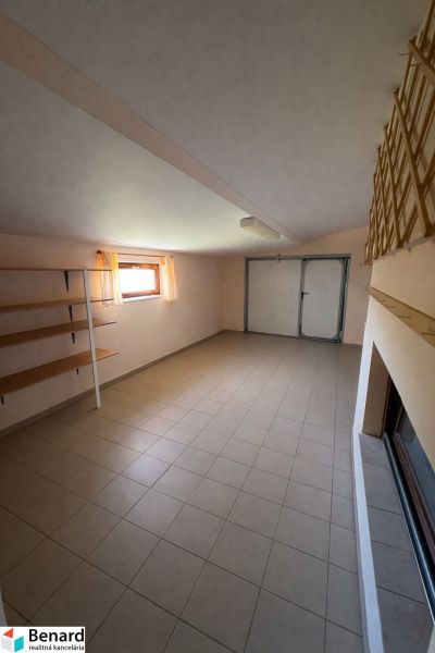 Innenraum eines Einfamilienhauses mit Fliesenboden, Stauregale und einem Fenster mit zarten Vorhängen.