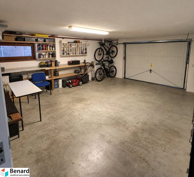 Eine Garage in einem Einfamilienhaus mit Klapprädern, einem Rasenmäher und Regalen für Werkzeuge.